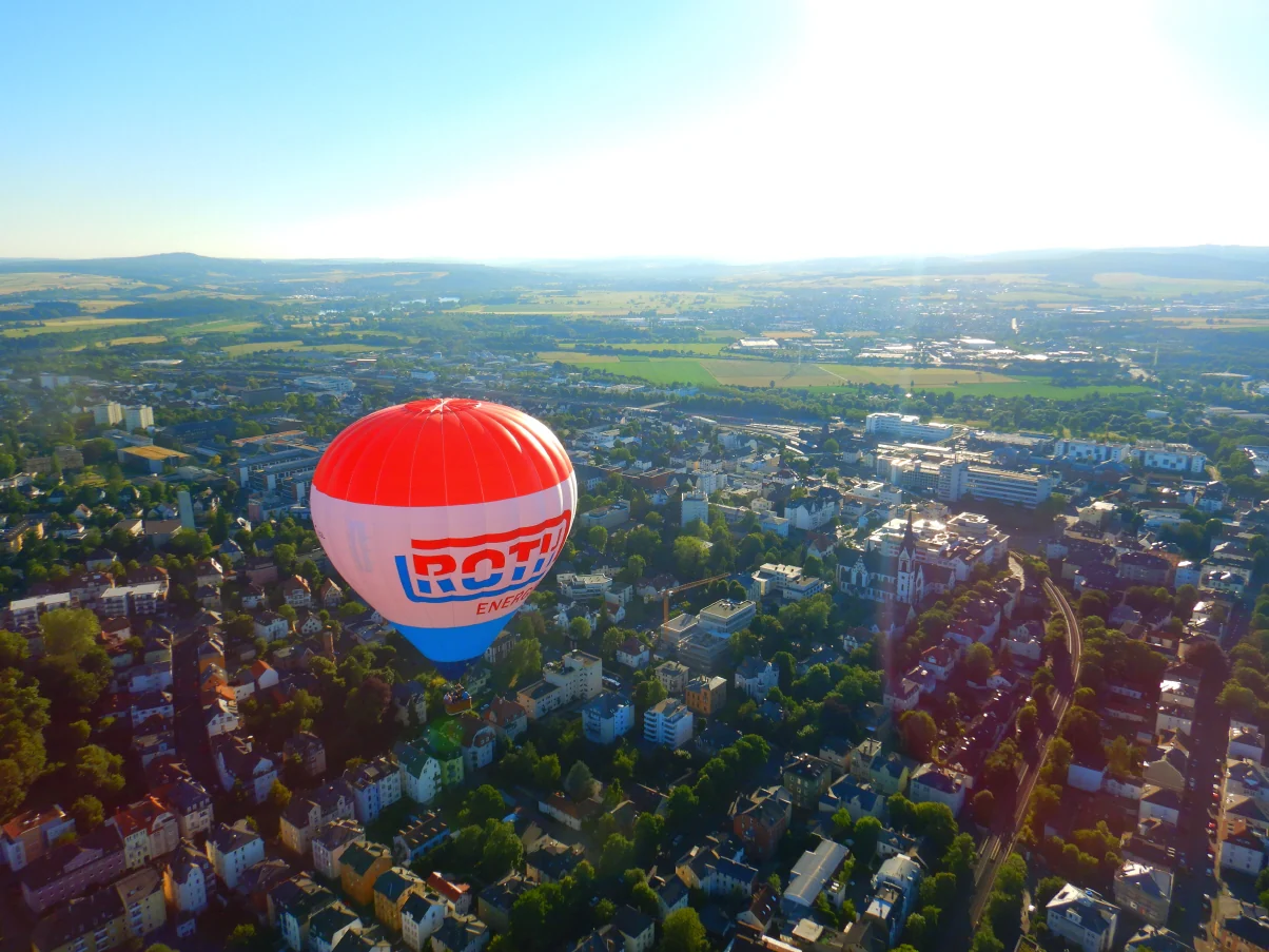 Der rot-blaue Roth-Ballon des Lahntal-Ballonteams über der grünen Landschaft und den Häusern Mittelhessens